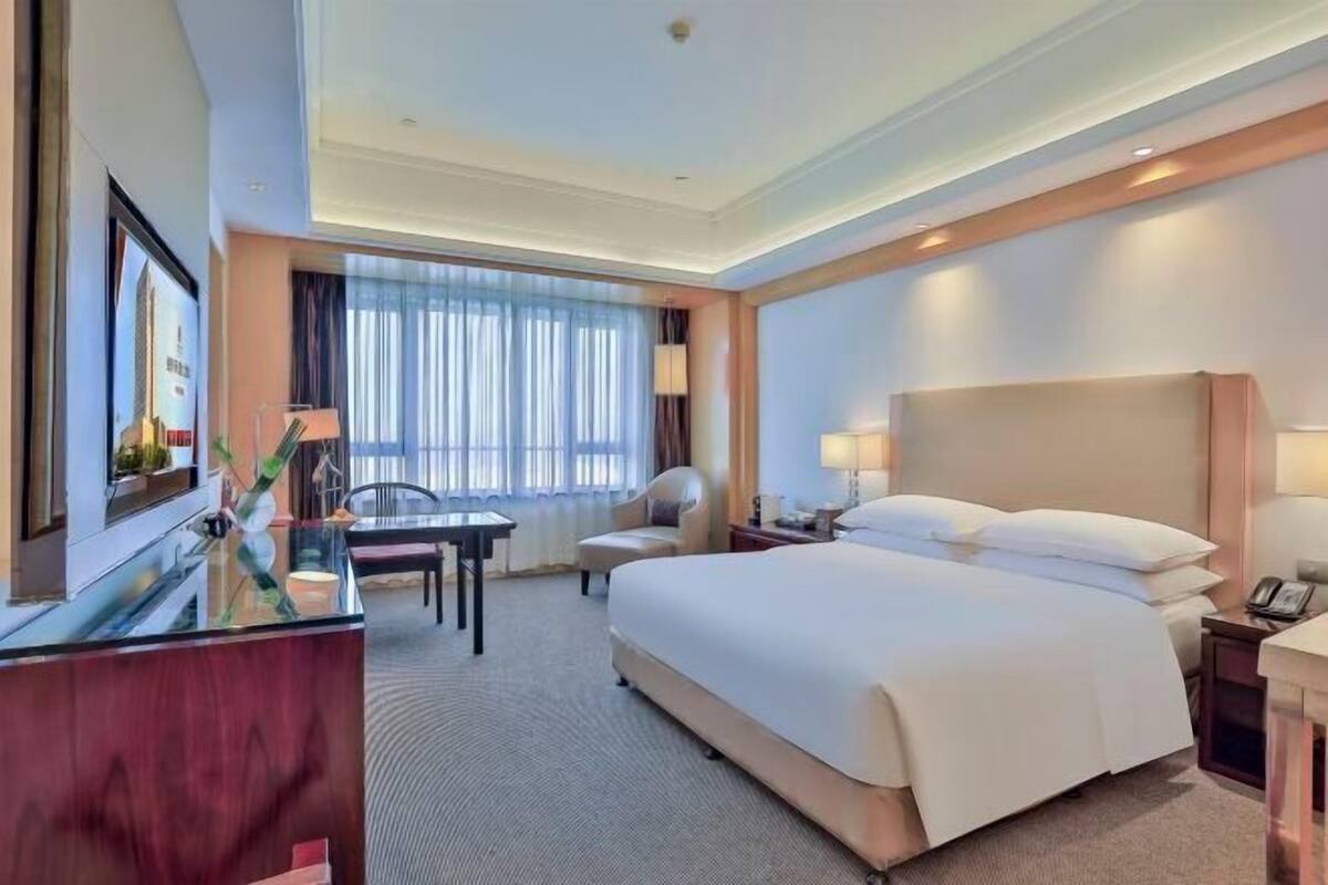 Une chambre d’hôtel avec un grand lit, un bureau, une chaise, une télévision et une fenêtre avec des rideaux.
