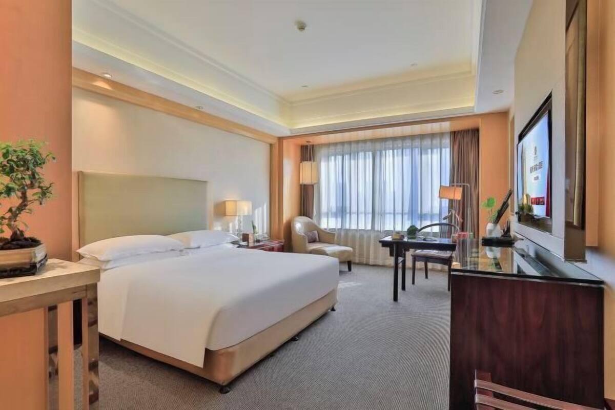 Une chambre d’hôtel avec un grand lit, un bureau, une chaise, une télévision et une fenêtre avec des rideaux.
