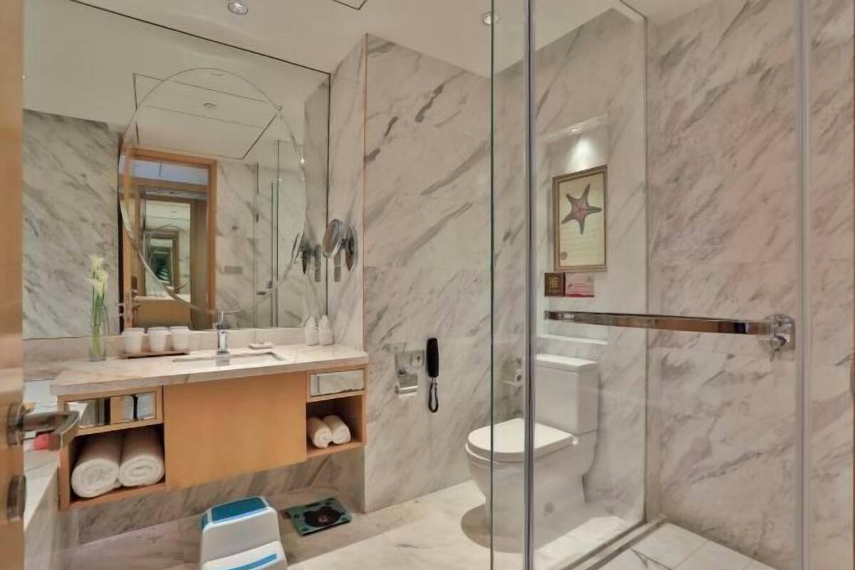 Une salle de bain moderne avec une douche à parois de verre, un mur recouvert de carreaux de marbre, un meuble-lavabo avec un miroir et des toilettes.