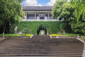 Un edificio tradicional con tejado de tejas, rodeado de abundante vegetación y una escalera de piedra que lleva a él.