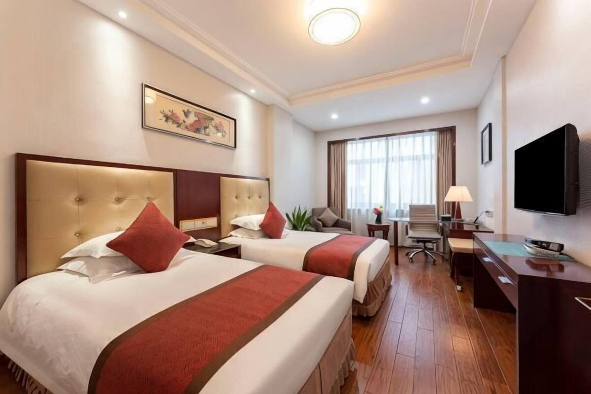 Habitación de hotel con dos camas, un escritorio, un televisor y una ventana con cortinas.