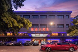 A hotel with a sign in a foreign language, multiple cars parked in front, and a red car in the foreground. - Yintai Hotel (Hometown of Luxun Shaoxing) (Shaoxing)