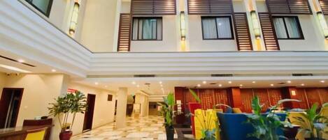 A hotel lobby with a checkered floor, multiple seating areas, and potted plants.
