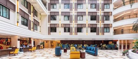 A hotel lobby with a checkered floor, multiple seating areas, and a central atrium with a view of the building's exterior.