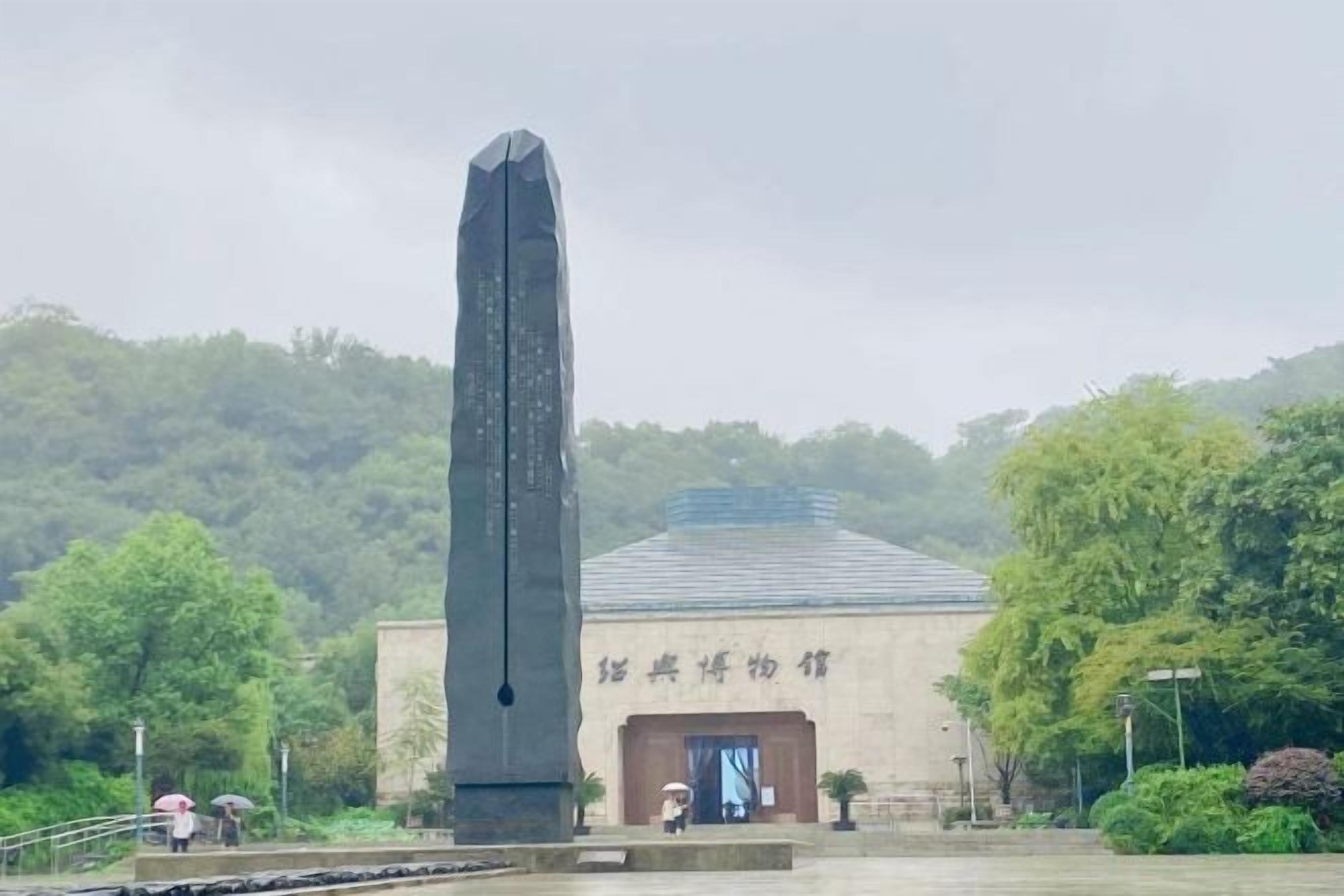 A tall monument in front of a building with a door and a sign.