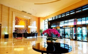 A hotel lobby with a reception desk, a large window, and a round table with a vase of flowers.