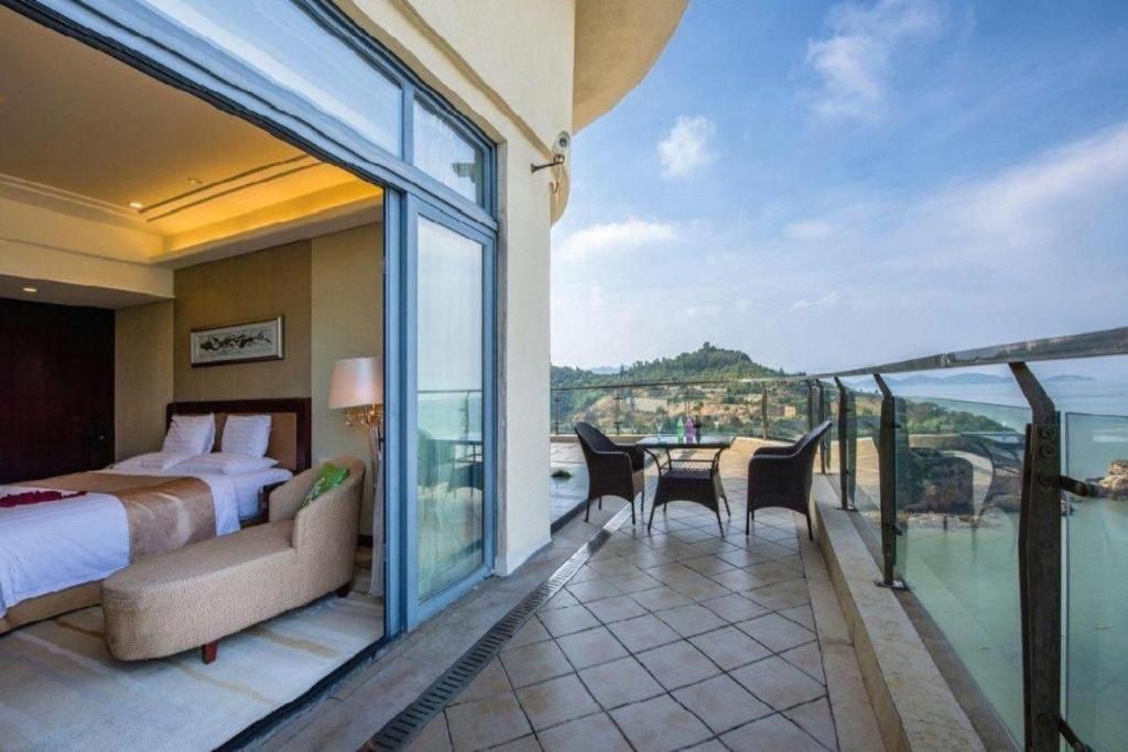 Une chambre d’hôtel avec un balcon, un lit, un canapé et une table avec des chaises.