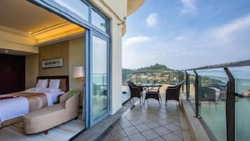 Une chambre d’hôtel avec un balcon, un lit, un canapé et une table avec des chaises.