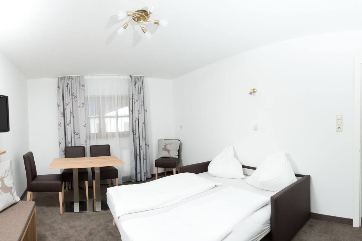 Una habitación de hotel con cama, escritorio, silla, televisor y ventilador de techo.