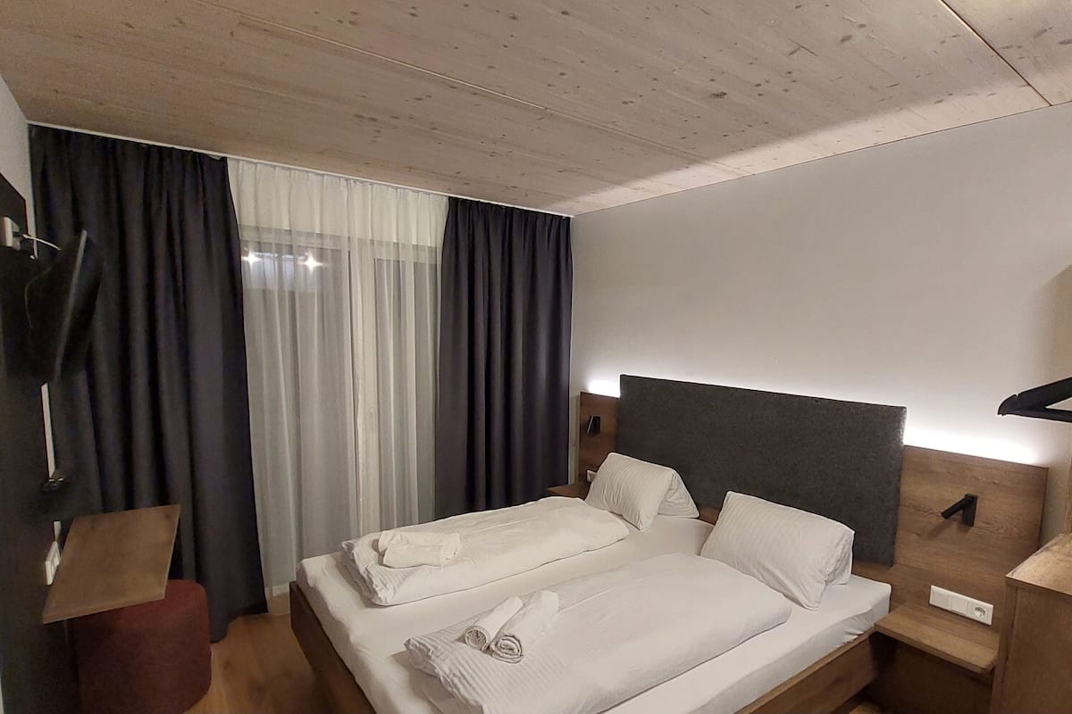 Una habitación de hotel moderna con una cama bien hecha, un cabecero de madera, una mesita de noche con una lámpara y un perchero.