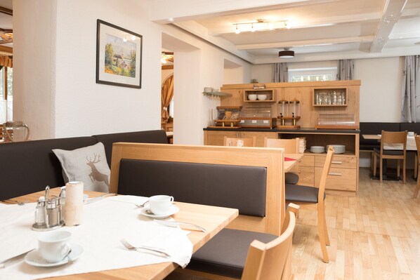 A cozy dining area with a wooden table and chairs, a bench, and a kitchen in the background. - Pension Irlingerhof (Tiefgraben)