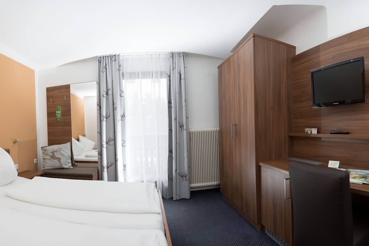 Habitación de hotel con cama, escritorio, televisión y baño visible a través de una puerta de vidrio.