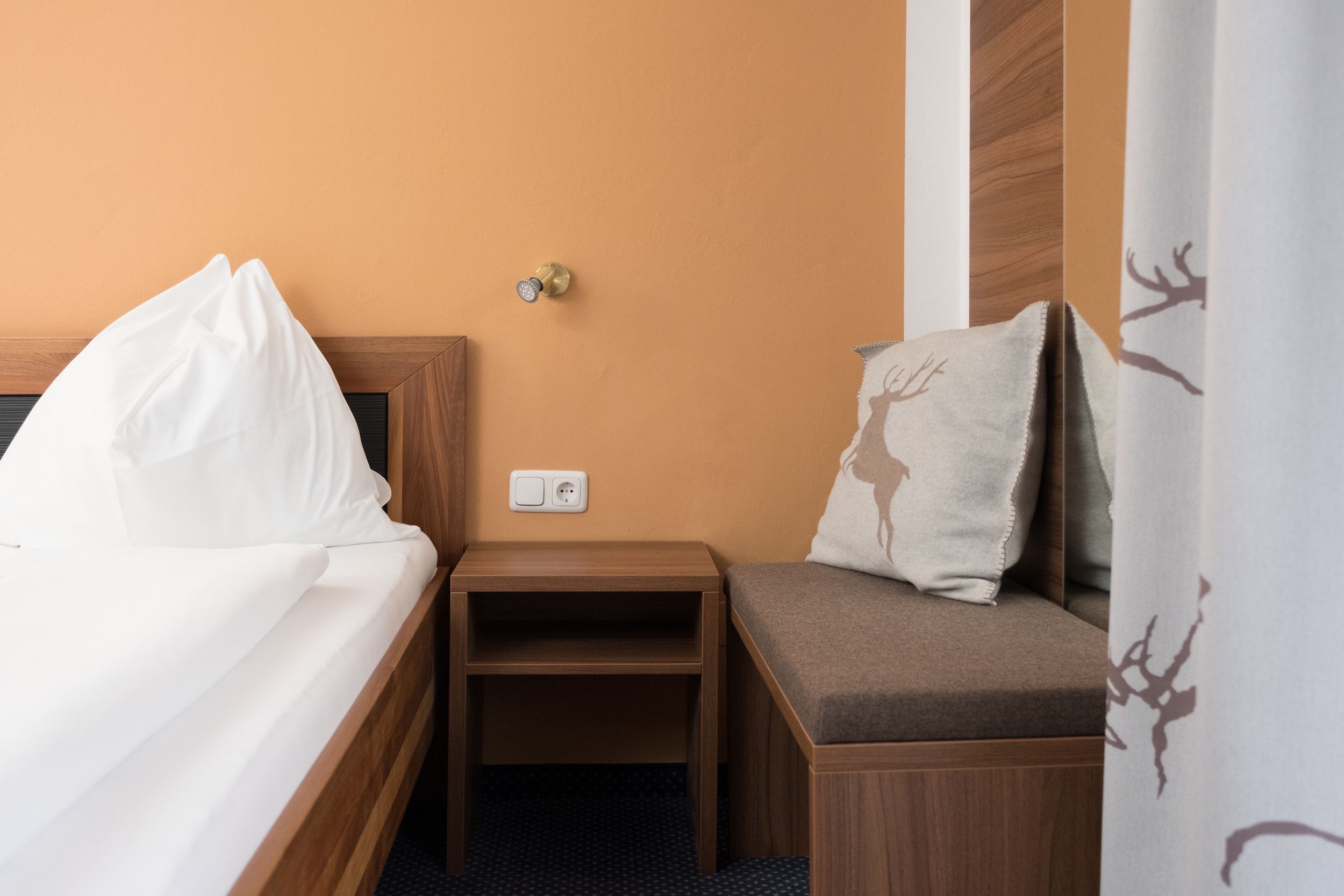 Habitación de hotel con cama, mesita de noche y zona de estar con cojín.
