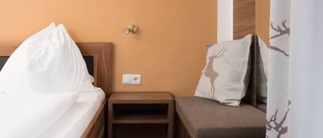 Habitación de hotel con cama, mesita de noche y zona de estar con cojín.