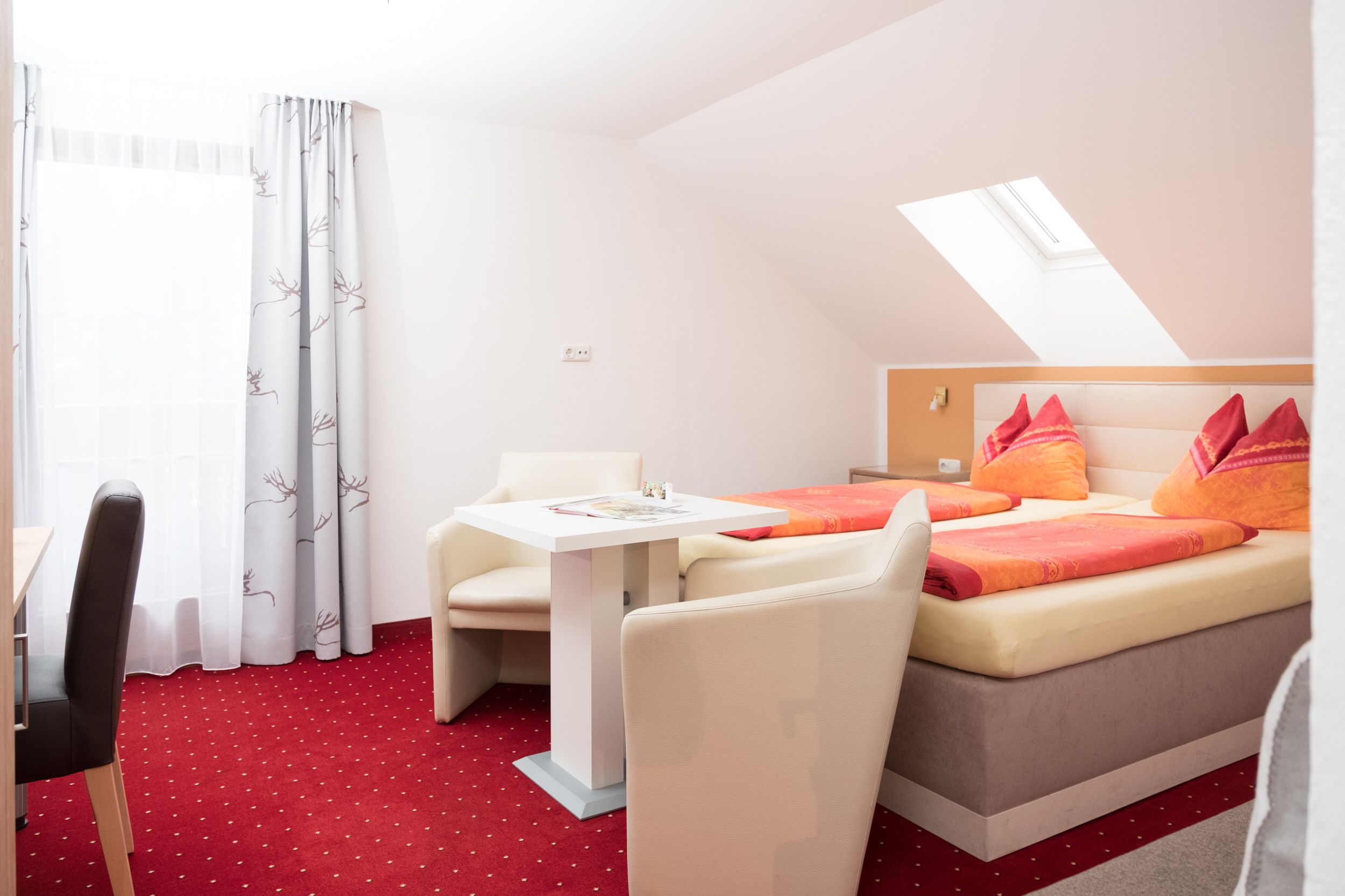 A hotel room with a bed, a table, a chair, and a window with curtains.