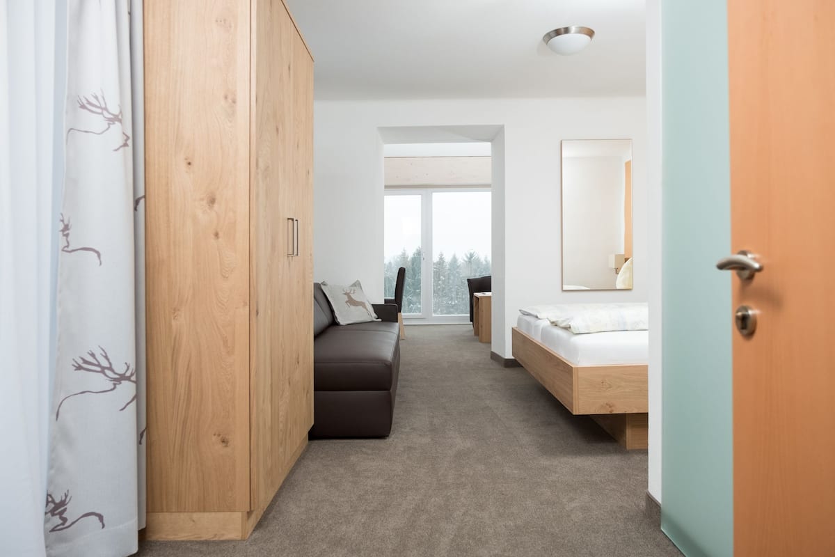Un dormitorio moderno con un armario de madera, un sofá, una cama y un ventanal grande.