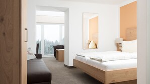 Ein modernes Hotelzimmer mit einem hölzernen Bett, einem großen Fenster, einer Couch und einem kleinen Tisch.