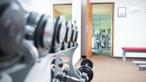 Ein Fitnessraum mit Trainingsgeräten, einer roten Bank und einer Tür zu einem anderen Raum.