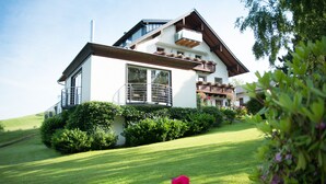 Ein modernes, zweistöckiges Haus mit geneigtem Dach, großen Fenstern und einem Balkon mit Pflanzen.