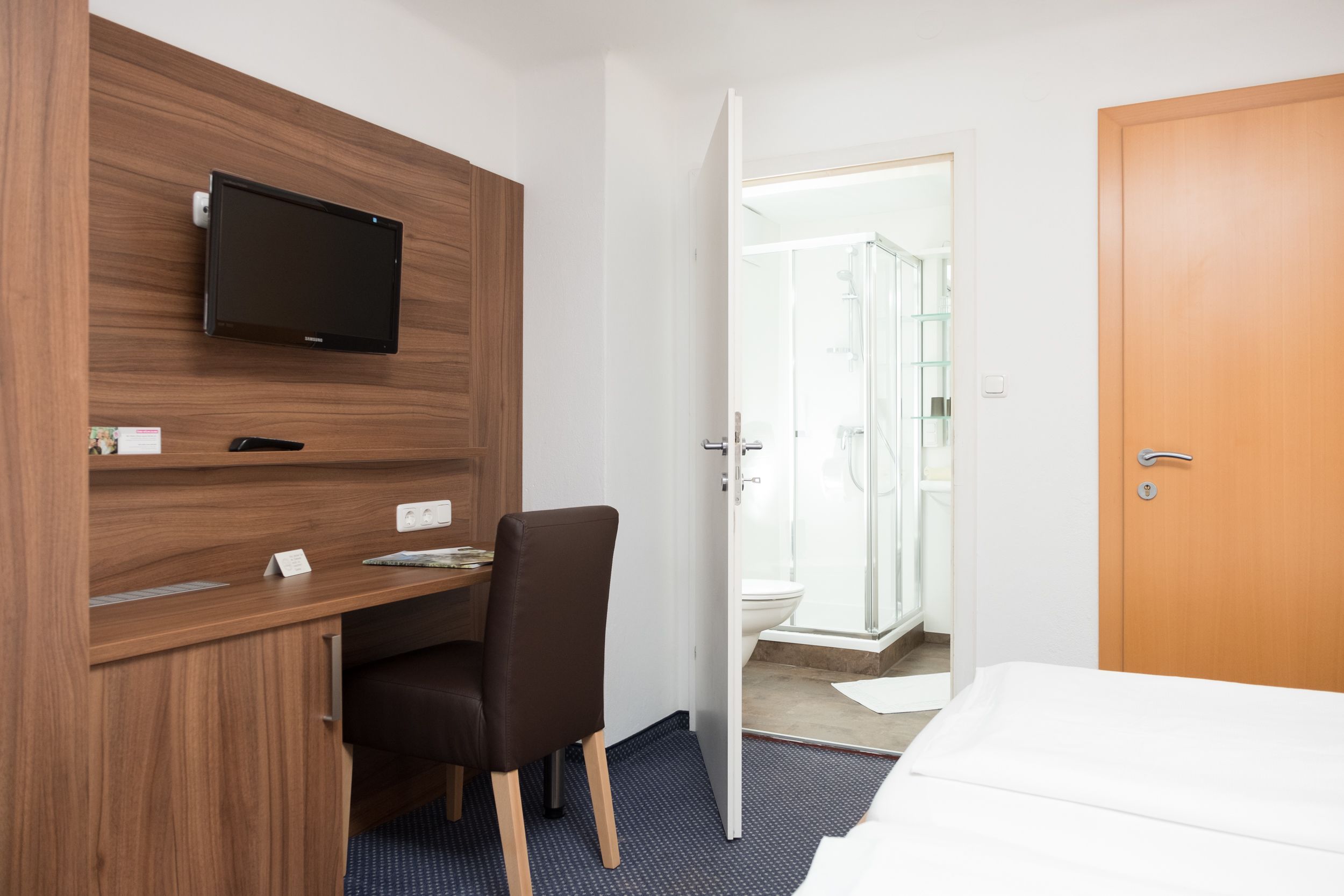 A hotel room with a wooden desk, a television, a shower area, and a bed.