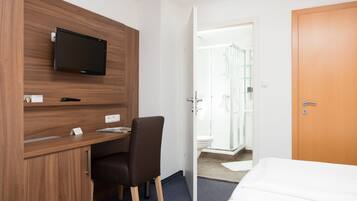 A hotel room with a wooden desk, a television, a shower area, and a bed.