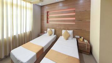 Two single beds with white bedding and beige throw pillows, accompanied by wooden nightstands and a shelf.