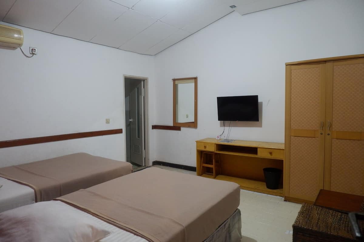 A hotel room with two single beds, a wooden desk with a television, a wardrobe, and a small trash bin.