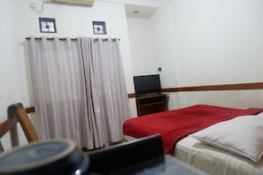 A hotel room with a bed, a TV on a stand, and a curtain. - Hotel Bali Indah (Bandung)