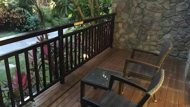 Una terraza de madera con un muro de piedra, barandilla y dos sillas de mimbre.