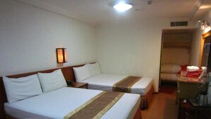 Habitación de hotel con dos camas individuales, una mesita de noche con lámpara, un armario y un escritorio pequeño con teléfono.