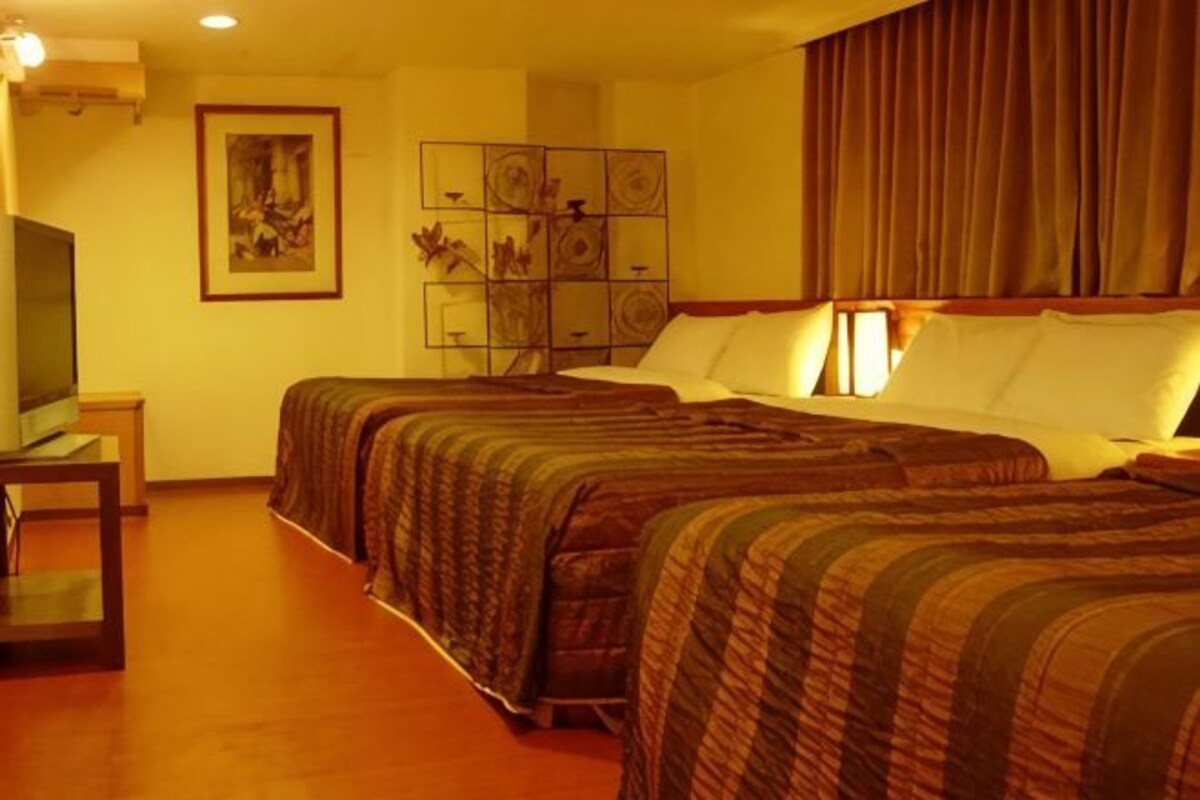 A hotel room with two beds, a television, a painting, and a decorative panel on the wall.
