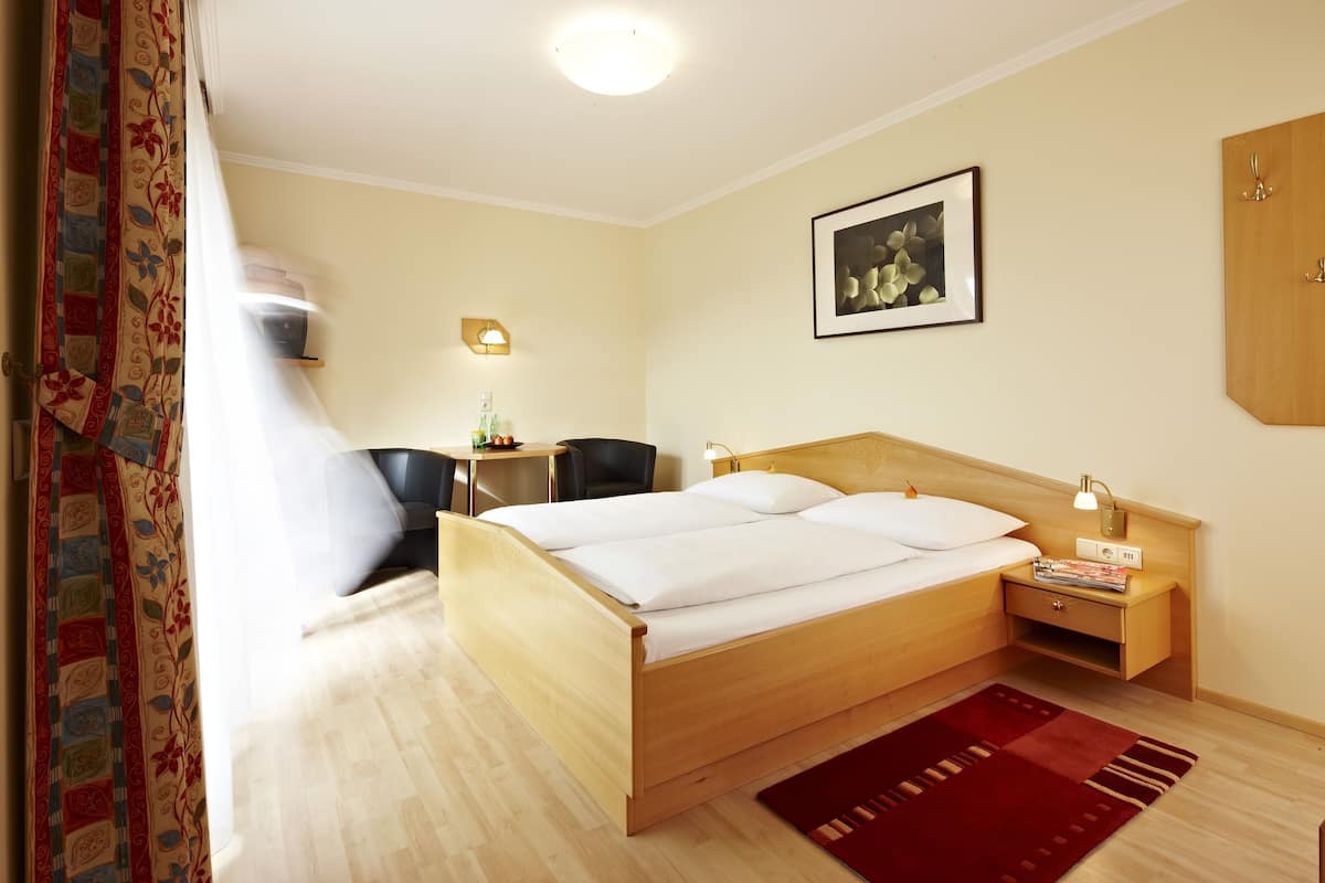 Una habitación de hotel con una cama de madera, un escritorio con una silla, una mesita con una lámpara y un cuadro enmarcado en la pared.