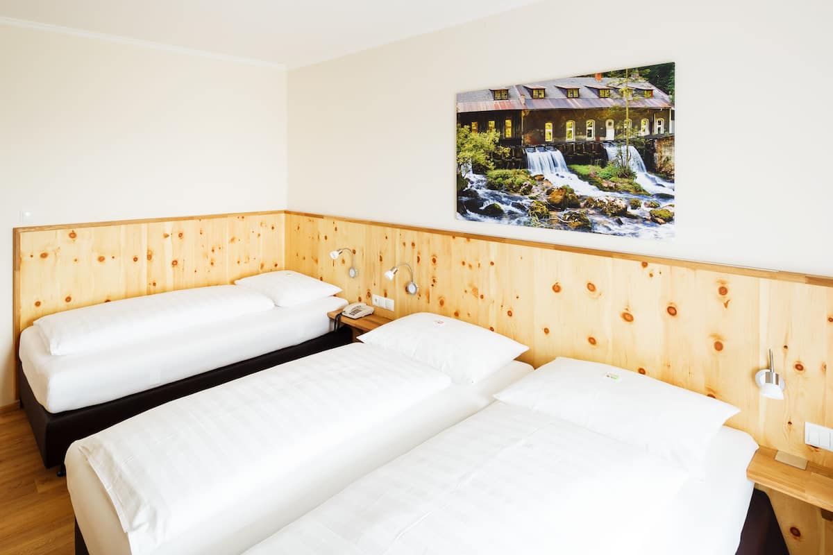 Habitación de hotel con dos camas, cabecera de madera, un cuadro de una cascada y piso de madera.