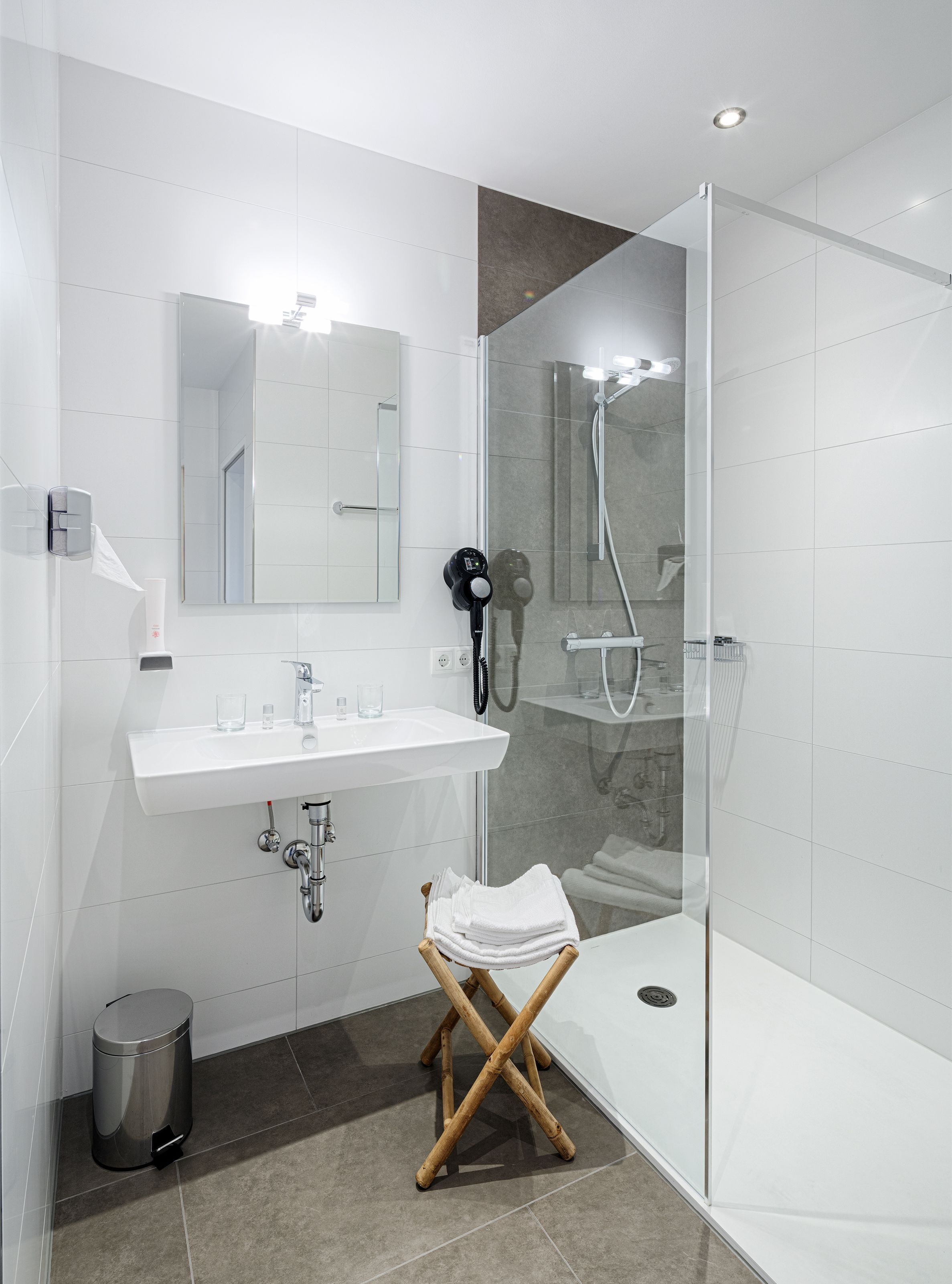 A modern bathroom with a white sink, mirror, and glass shower enclosure.