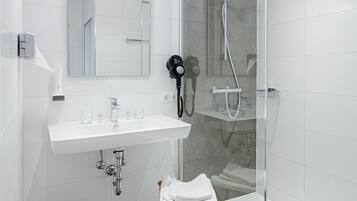 Un baño moderno con lavamanos blanco, espejo y cabina de ducha con vidrio.