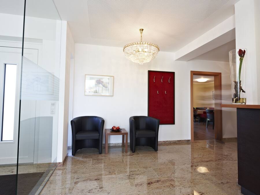 Una hall moderna con un lampadario, due poltrone nere, un tavolino con un fiore rosso e una parete decorata in rosso.
