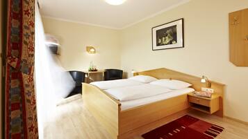 A hotel room with a wooden bed, a desk with a chair, a small table with a lamp, and a framed picture on the wall.