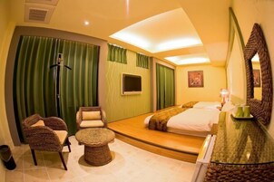 Una habitación de hotel con una cama, una zona de estar con una silla y una mesita, un espejo y un televisor.