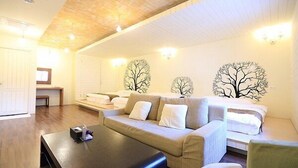 Et hyggeligt rum med sofa, seng og sofabord. Væggen er dekoreret med kunst, og der er en bænk.