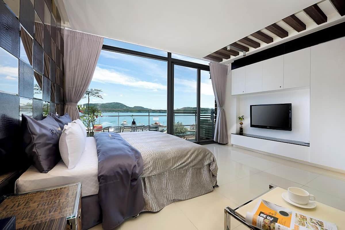 Ein modernes Hotelzimmer mit einem großen Bett, einem Flachbildfernseher und einem Balkon mit Blick auf das Wasser.