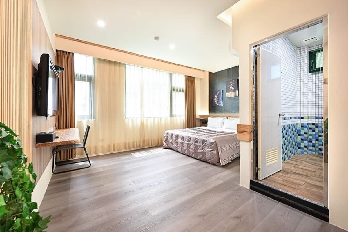 Ein modernes Hotelzimmer mit einem Bett, einem Schreibtisch mit Stuhl, einem Fernseher und einem großen Fenster mit Vorhängen.