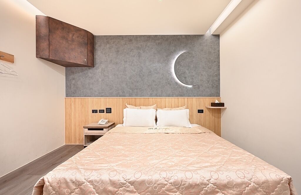 Habitación de hotel con cama, cabecero de madera, mesita de noche, decoración de luna creciente en la pared y armario de madera.
