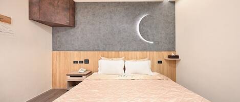 Habitación de hotel con cama, cabecero de madera, mesita de noche, decoración de luna creciente en la pared y armario de madera.