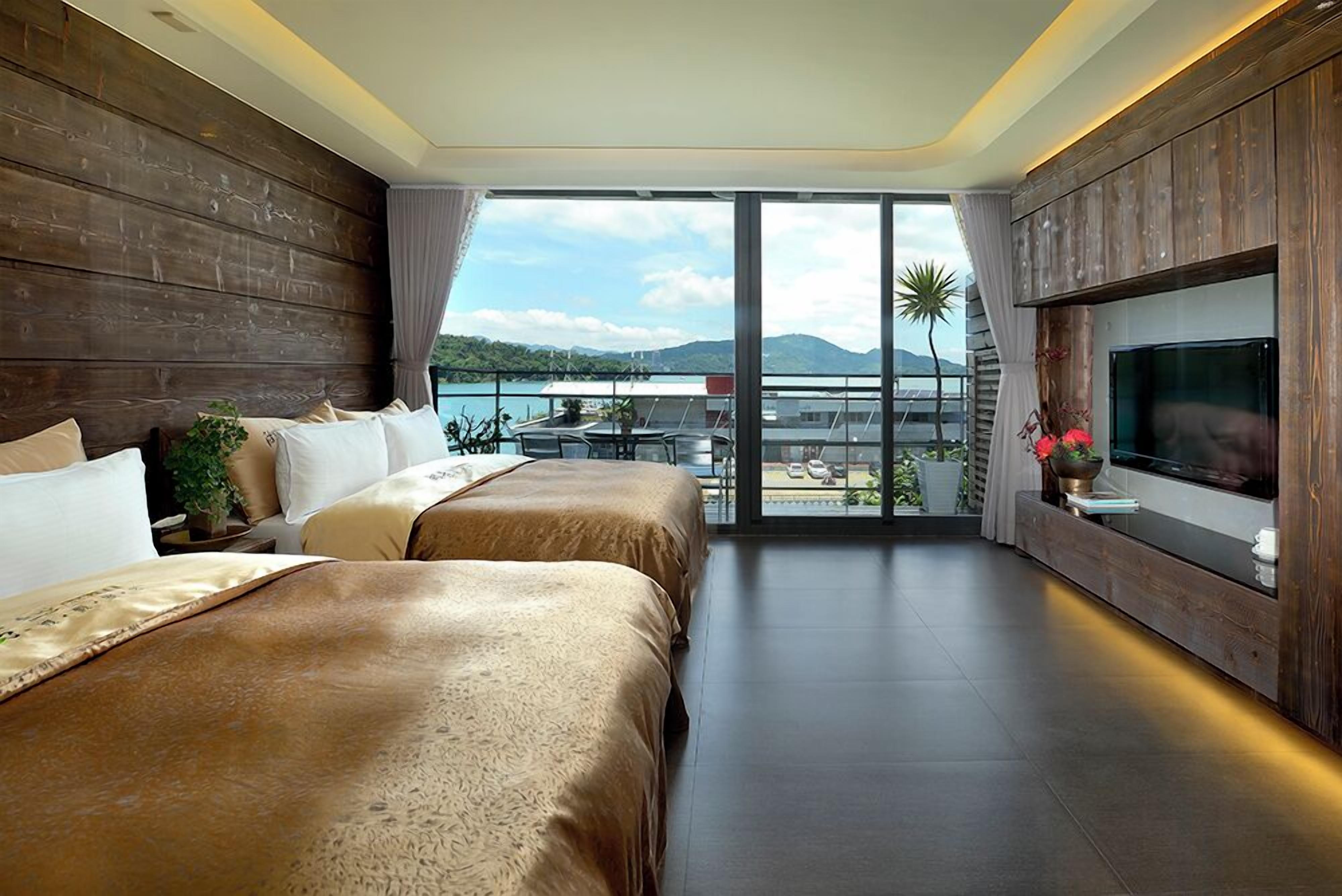 A modern hotel room with a large bed, a TV, and a balcony with a view of the mountains.