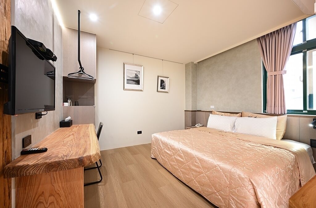 A bedroom with a bed, a desk, a TV, and a window with curtains.