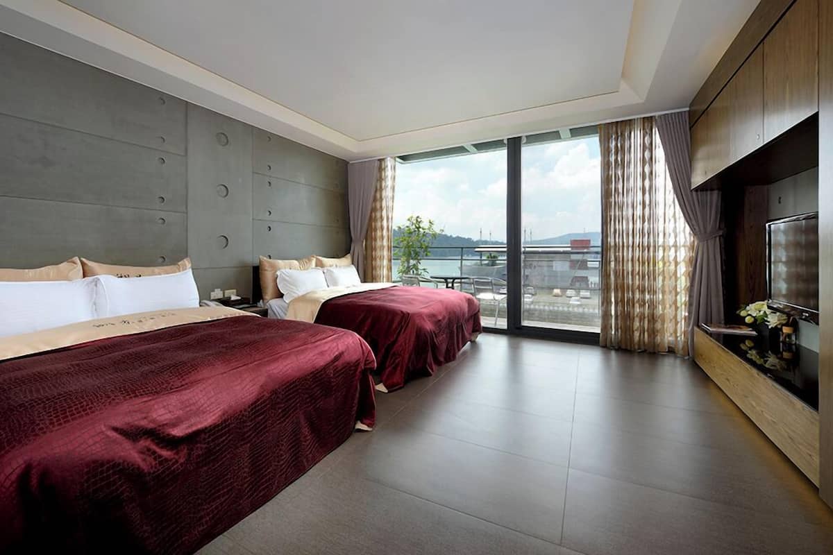 Ein Hotelzimmer mit zwei Betten, einem großen Fenster mit Vorhängen, einem Fernseher und Blick auf die Stadt.