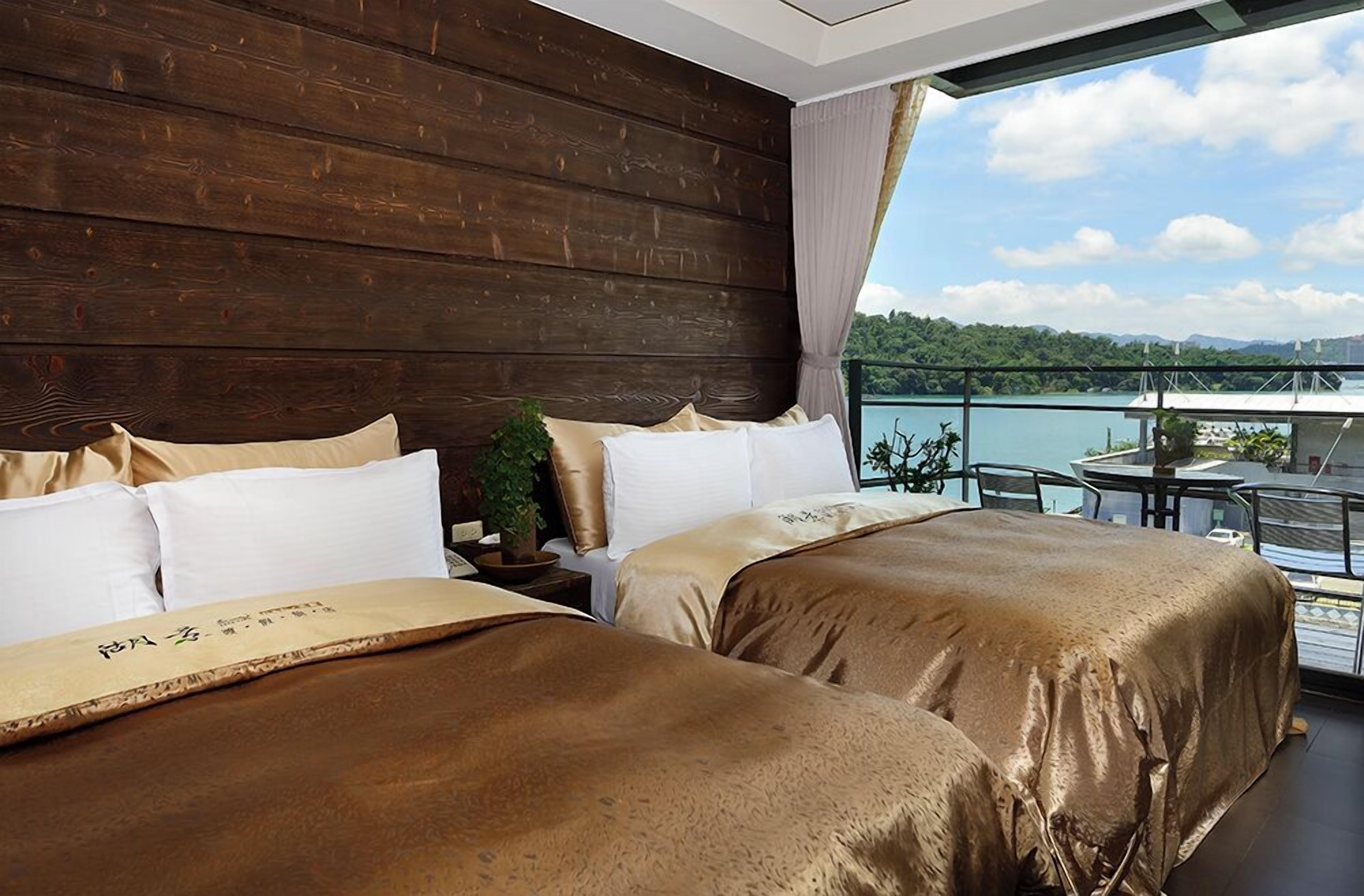 A hotel room with two beds, a view of a lake, and a balcony with a table and chairs.