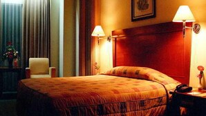 A hotel room with a large bed, two bedside lamps, a wooden headboard, a chair, and a desk with a telephone. - Nalendra (Bandung)