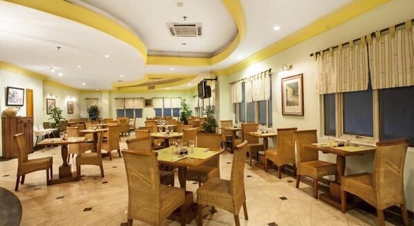 A dining area with multiple tables and chairs, air conditioning, and framed pictures on the walls. - Nalendra (Bandung)