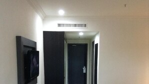 Habitación de hotel pequeña con televisor montado en la pared, un escritorio, una cama y una puerta que da a otra habitación.